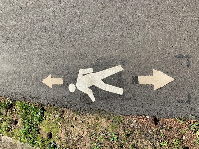 A white pedestrian logo with arrows pointing opposite directions on pavement