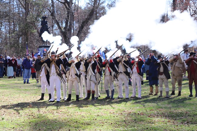 Revolutionary War reenactors fire muskets creating cloud of smoke