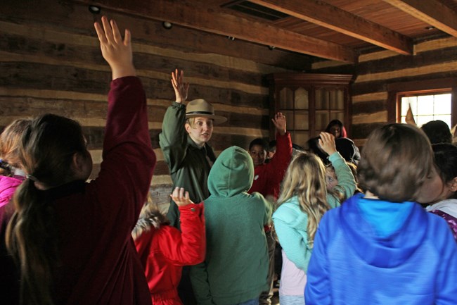 Ranger and kids raise their hands Park Ranger and students raise hands inside a historic log house