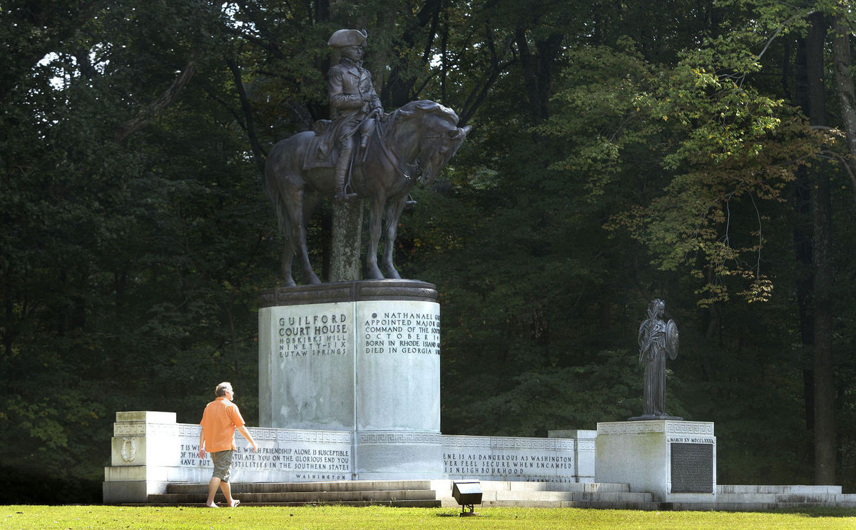 Visitor walks in front of Greene Monument Man in orange shirt walks in front of the equestrian monument to Maj. General Nathanael Greene