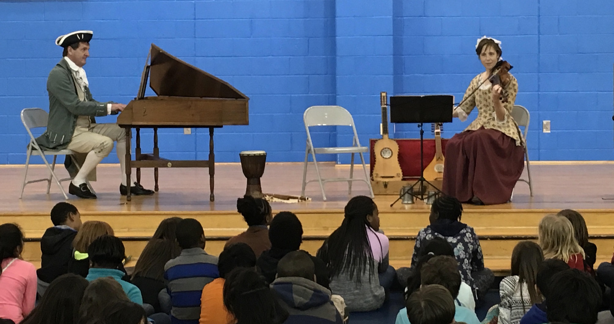 Two living history musicians play the piano forte and violin for a crowd of students