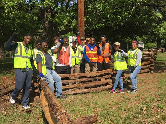 Twelve volunteers and park staff stand in front of a split rail fence, raising their arms in successful pose