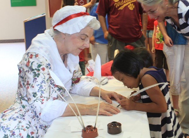 Child learning how to write with a quill pen Living History Interpreter woman teaches child how to write with a quill pen