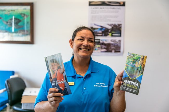 A park volunteer holds up two park brochures for the camera.