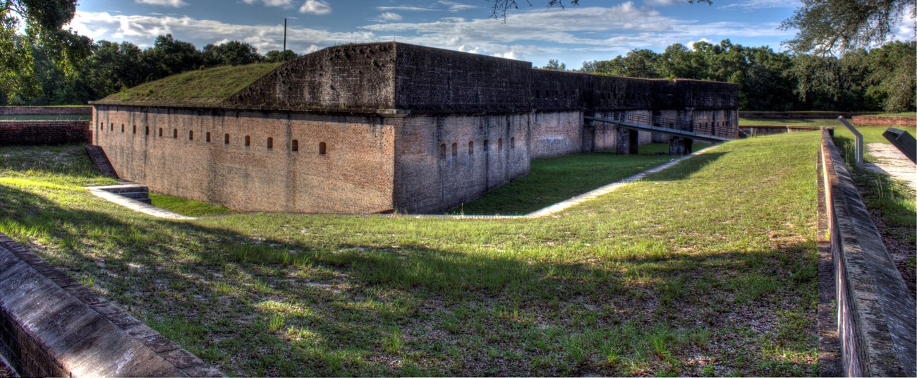 A historic masonry fort stands in a terraced field of green grass.