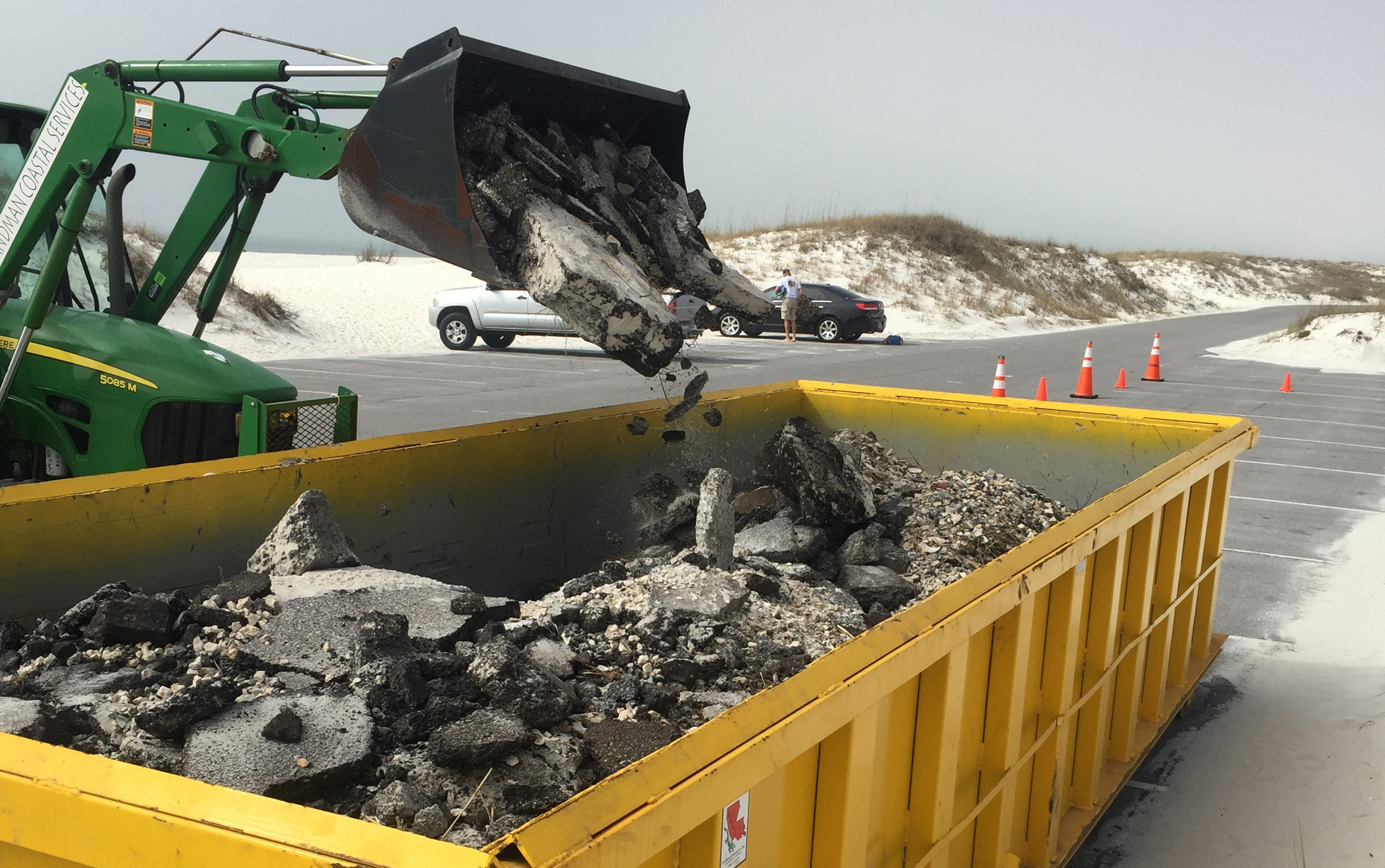Asphalt Removal A front-end load drops asphalt debris into a large dumpster.