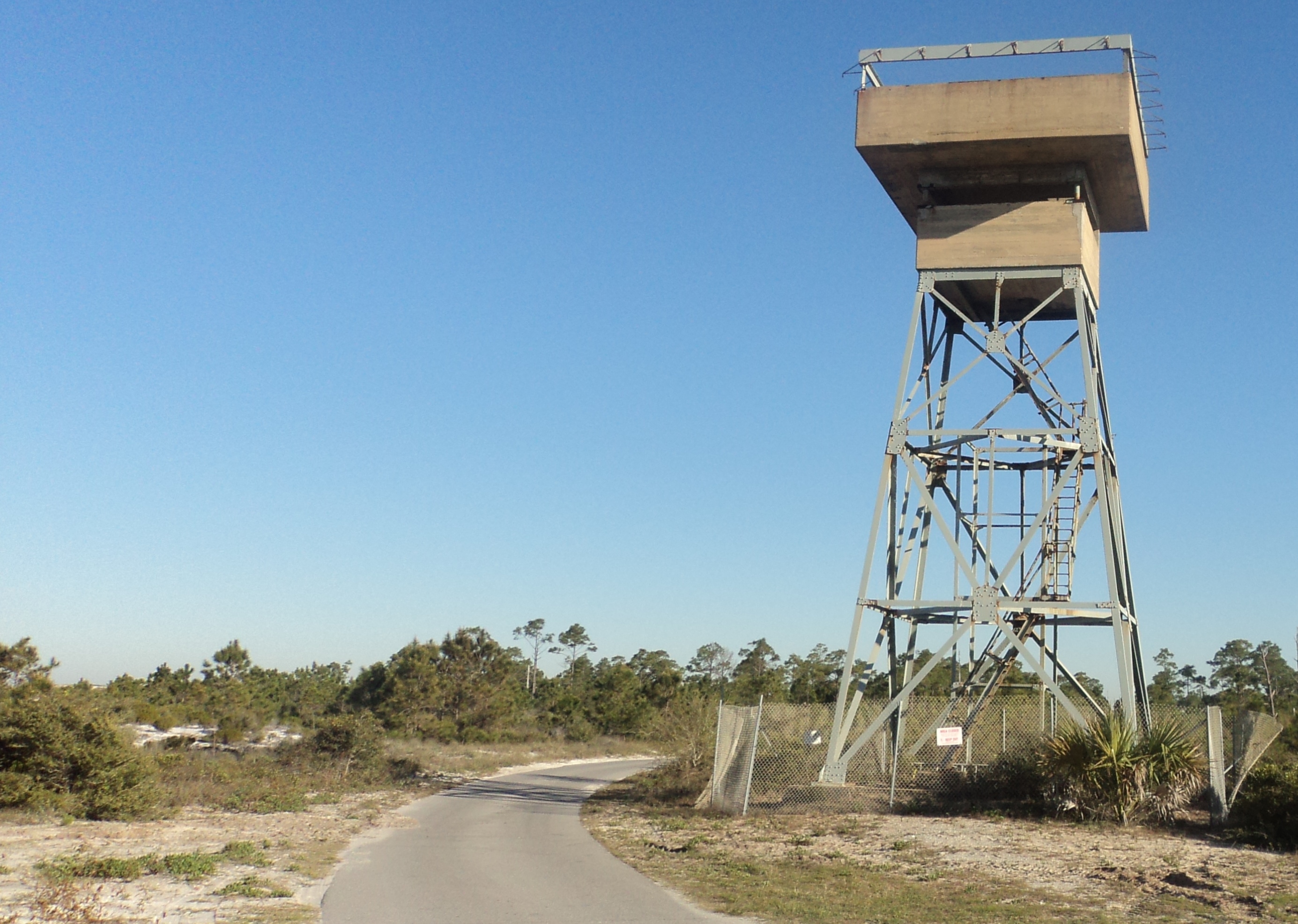 A steel and concrete tower stand near a one lane asphalt road.