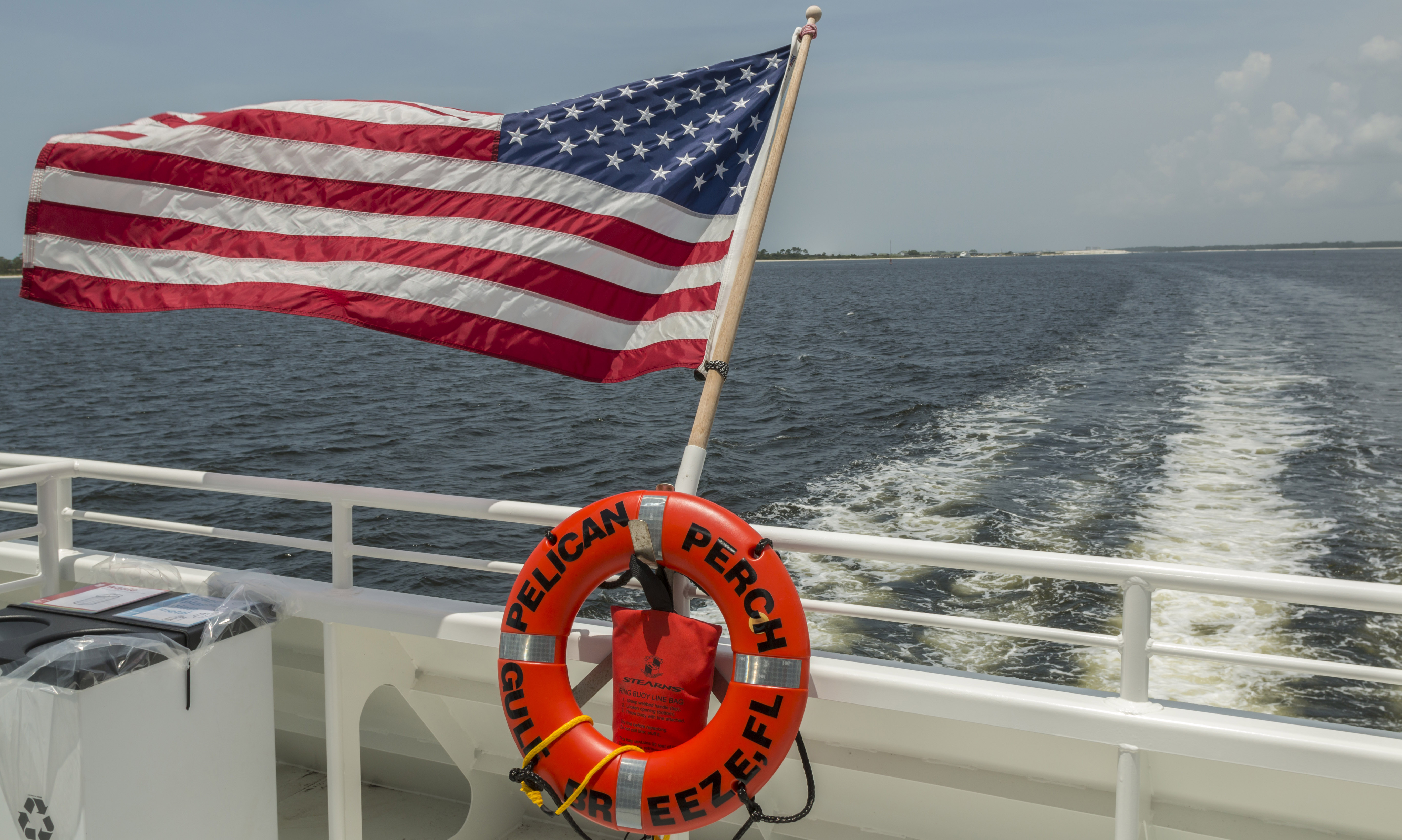 An american flag flys from the back of a tour boat.