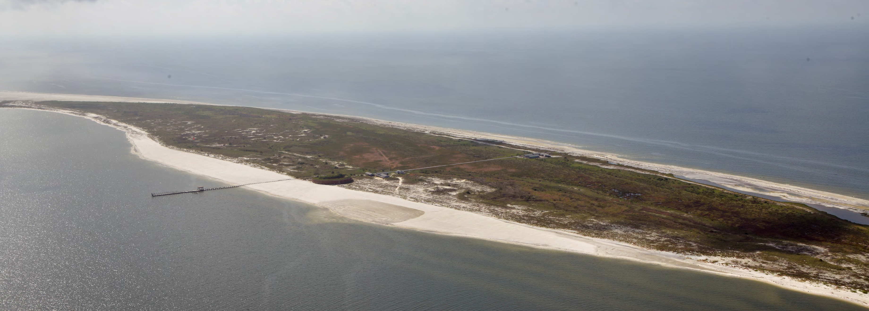 Aerial photo of an island with a pier extending off and several buildings toward the center. Aerial photo of an island with a pier extending off and several buildings toward the center.
