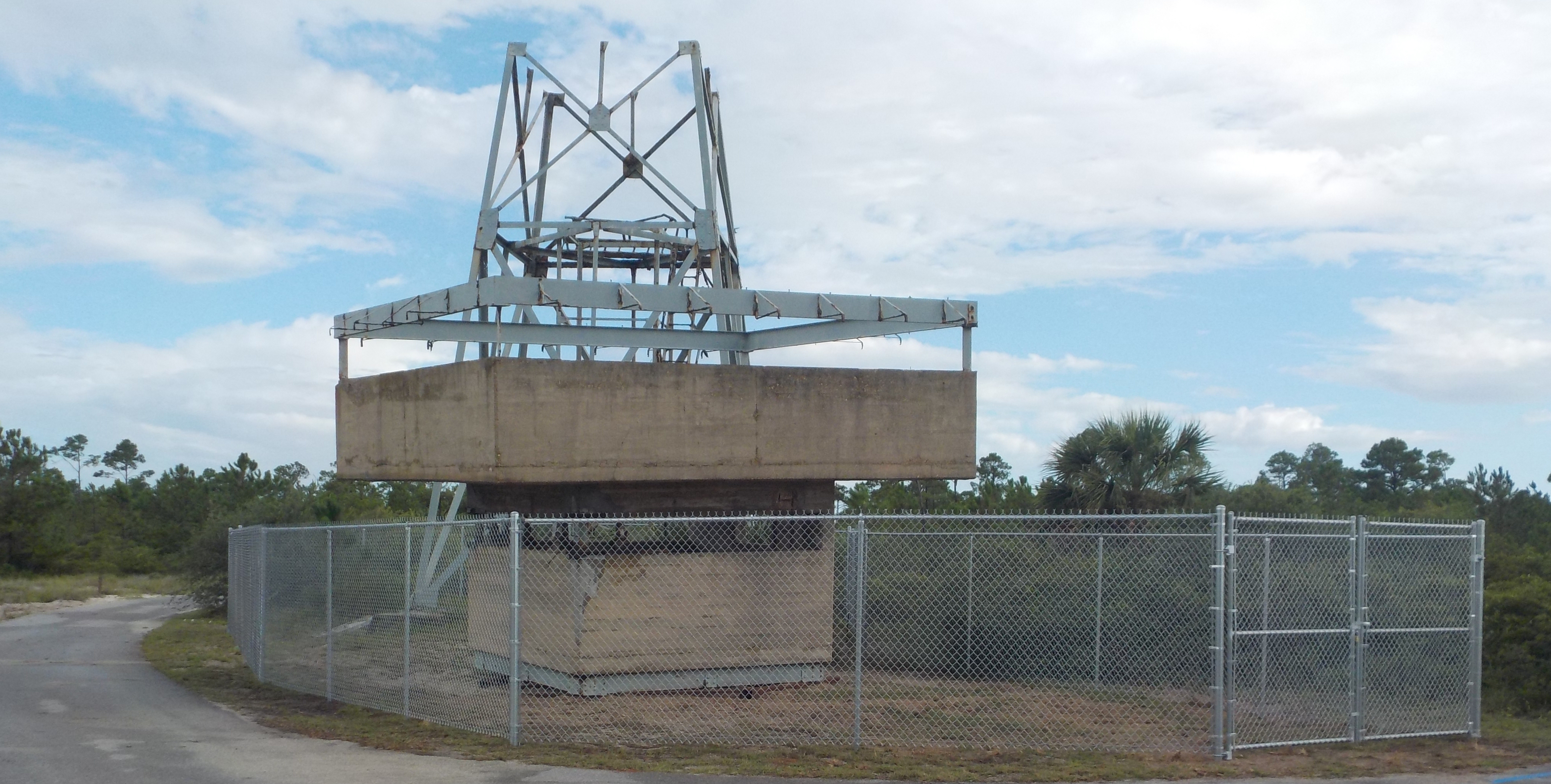 A concrete structure sits in front of a steel tower with trees in the background. A concrete structure sits in front of a steel tower with trees in the background.