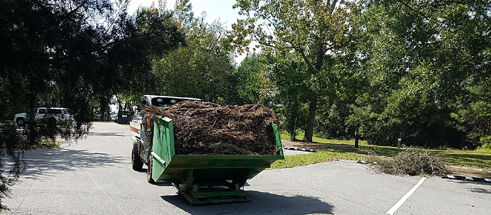 Davis Bayou Clearing Work Following Hurricane Nate Debris is stacked to the edge of a small piece of heavy equipment.