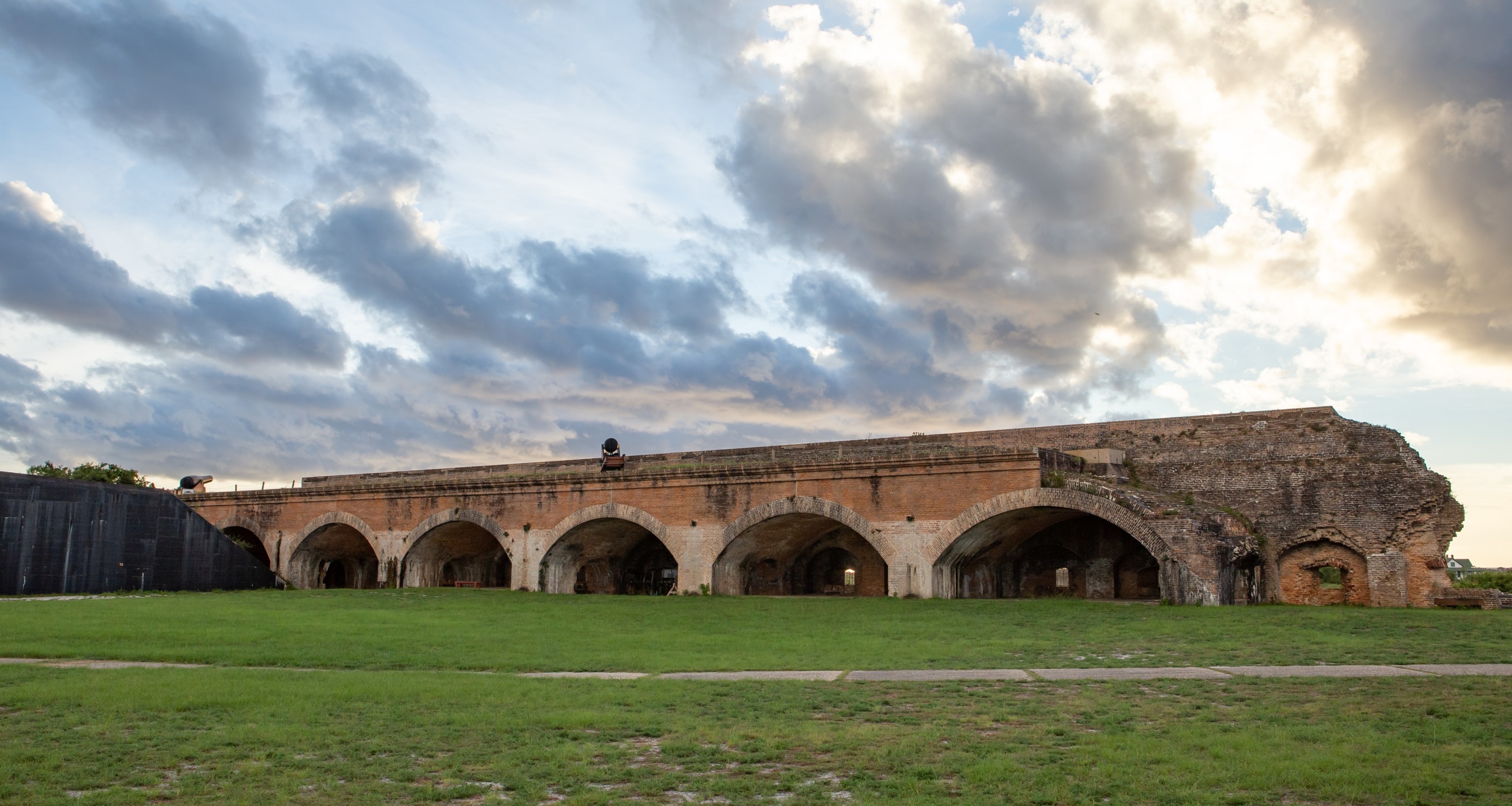 Brick exterior walls of Fort Pickens. Green grass in the foreground and blue sky and clouds in the background.