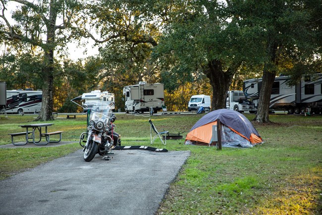 A motorcycle stands at a grassy campsite.