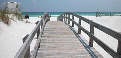 A gray wooden boardwalk crosses over the white sand dunes to the gulf beach. A gray wooden boardwalk crosses over the white sand dunes to the gulf beach.