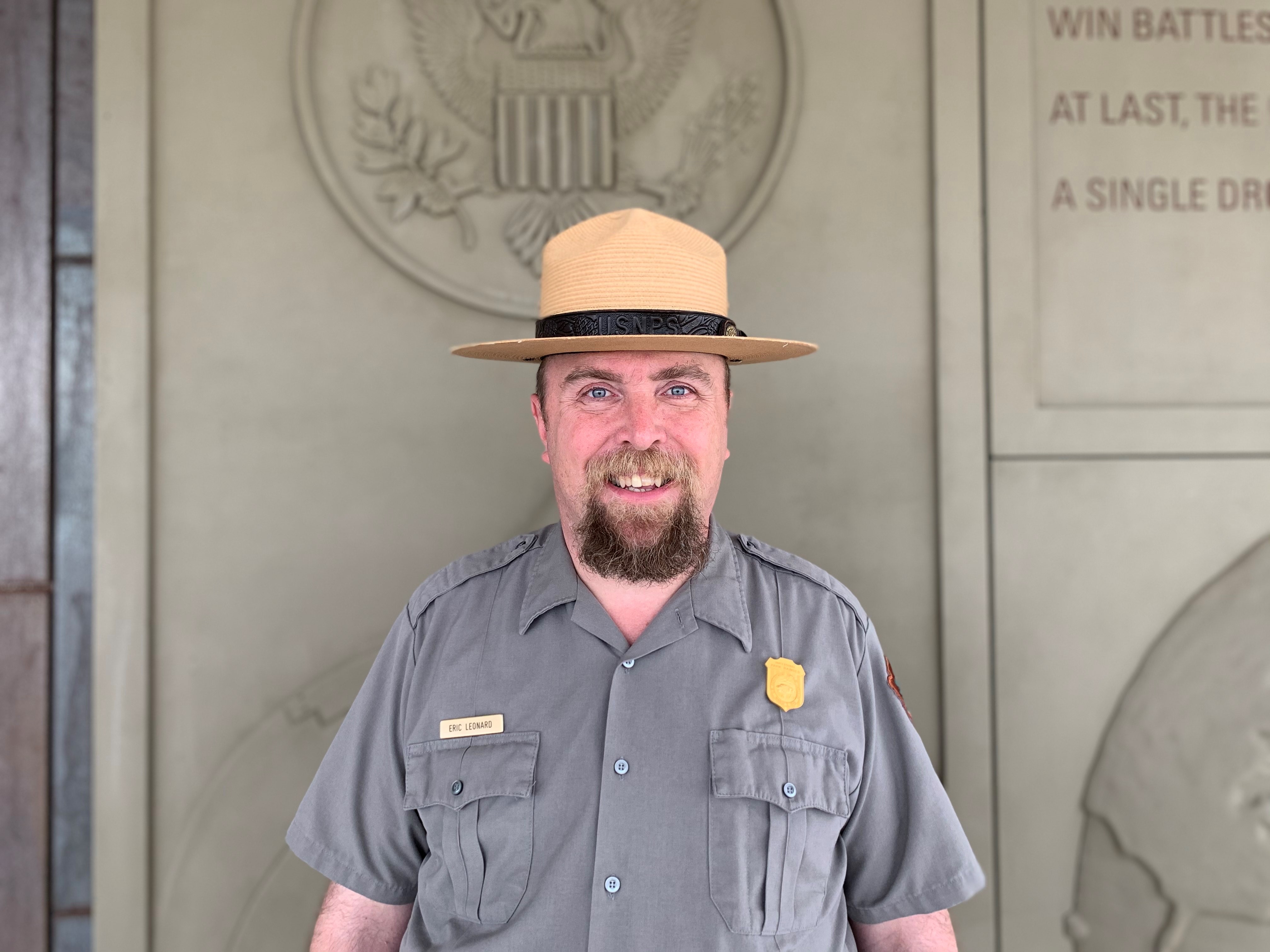 A man in uniform and hat stands before a concrete sculpture.