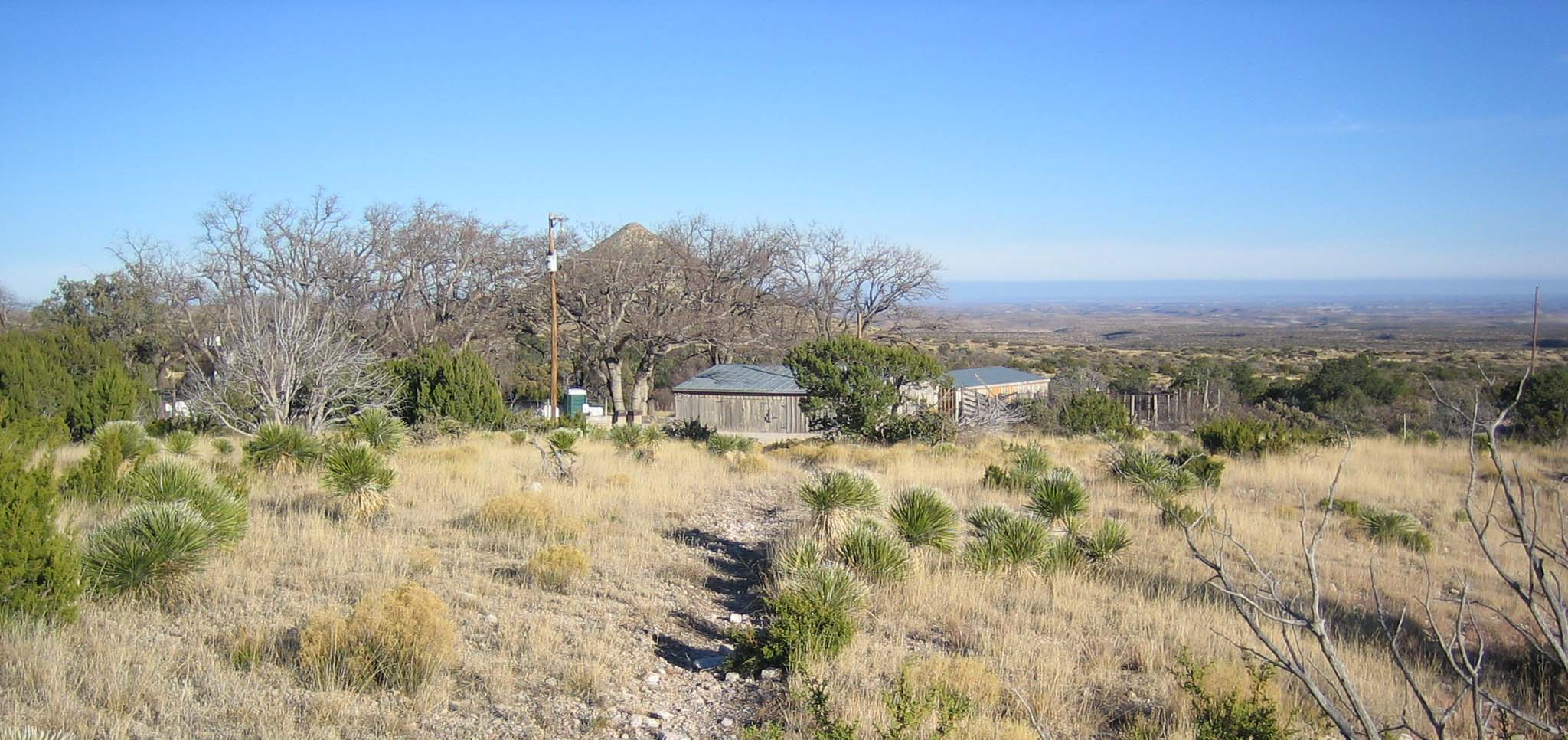 A rocky trail leads to a ranch compound in a desert landscape.