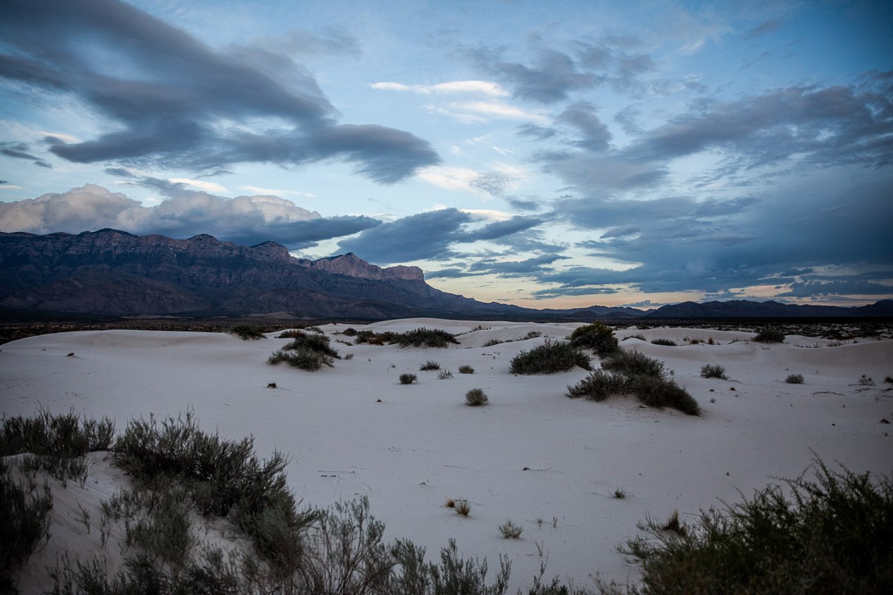 White sand dunes in front of a distant tall mountain face