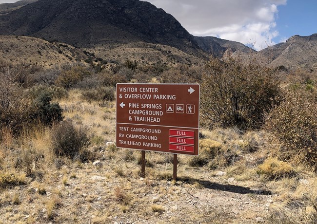 A brown directional sign with red notations of parking and campgrounds full