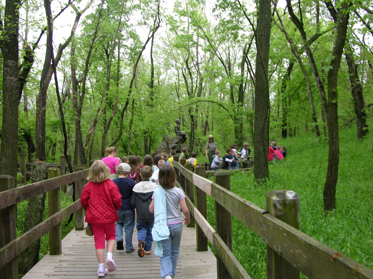 School children on the Carver trail during a field trip. A park ranger is leading the group. Also in the image is a bronze statue of young George Washington Carver.