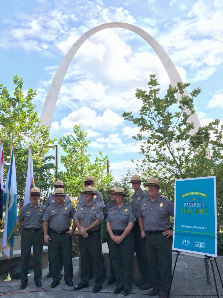 Nine white individuals in National Park Service uniforms, standing in front of the Gateway Arch in St. Louis, Missouri.