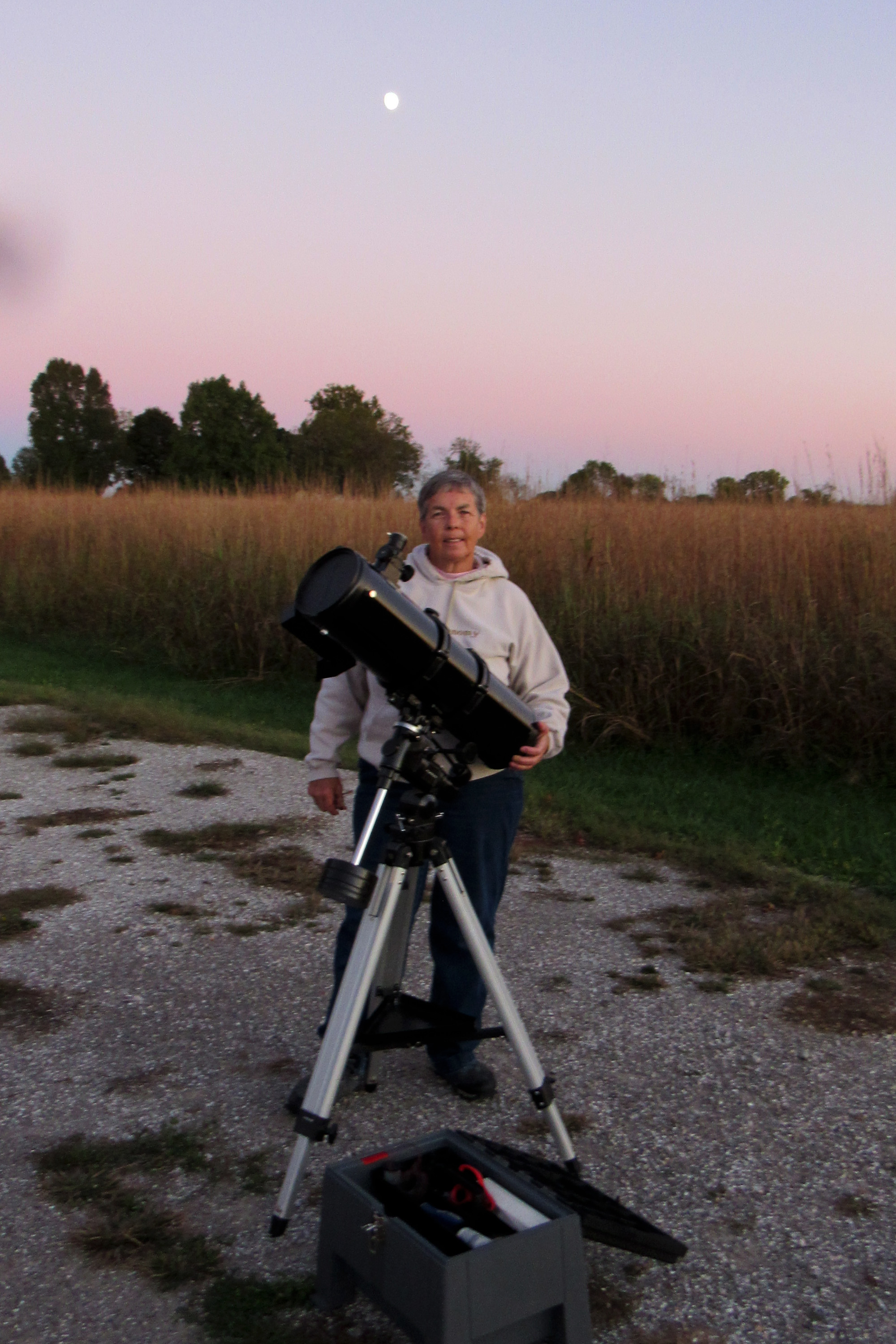 A woman with a large telescope outside.