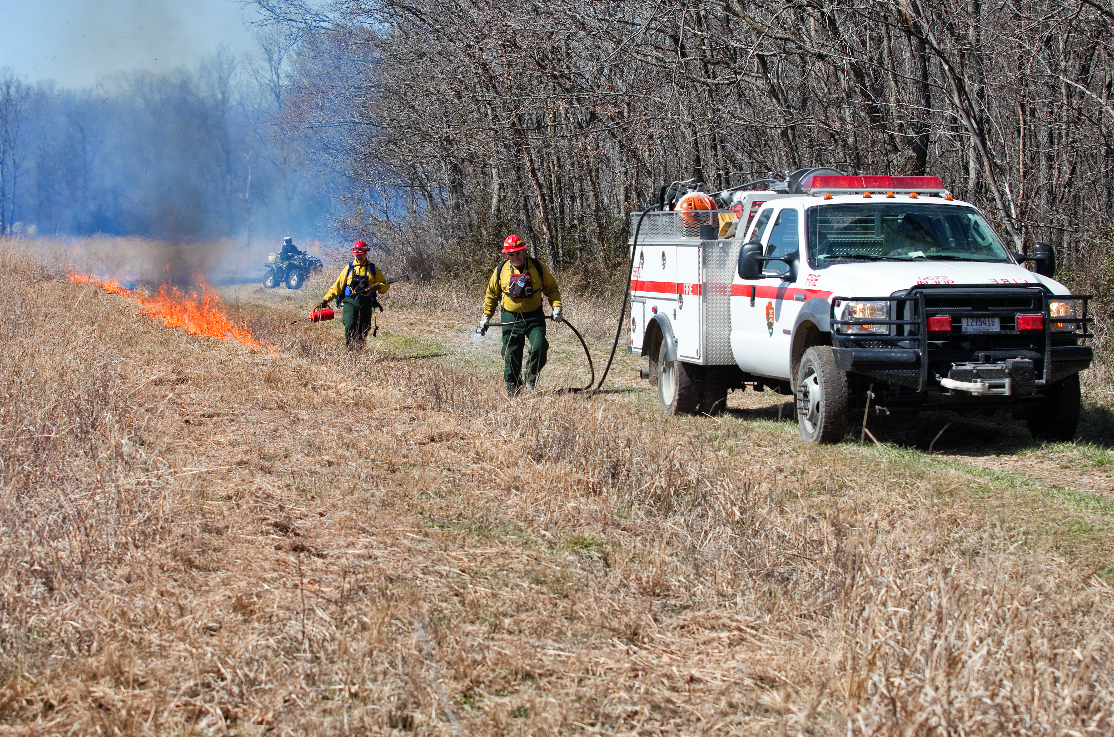 Prescription burn at the park. Two park service employees conducting a prescribed burn at the park service. A red and white park service truck is also in the photograph.