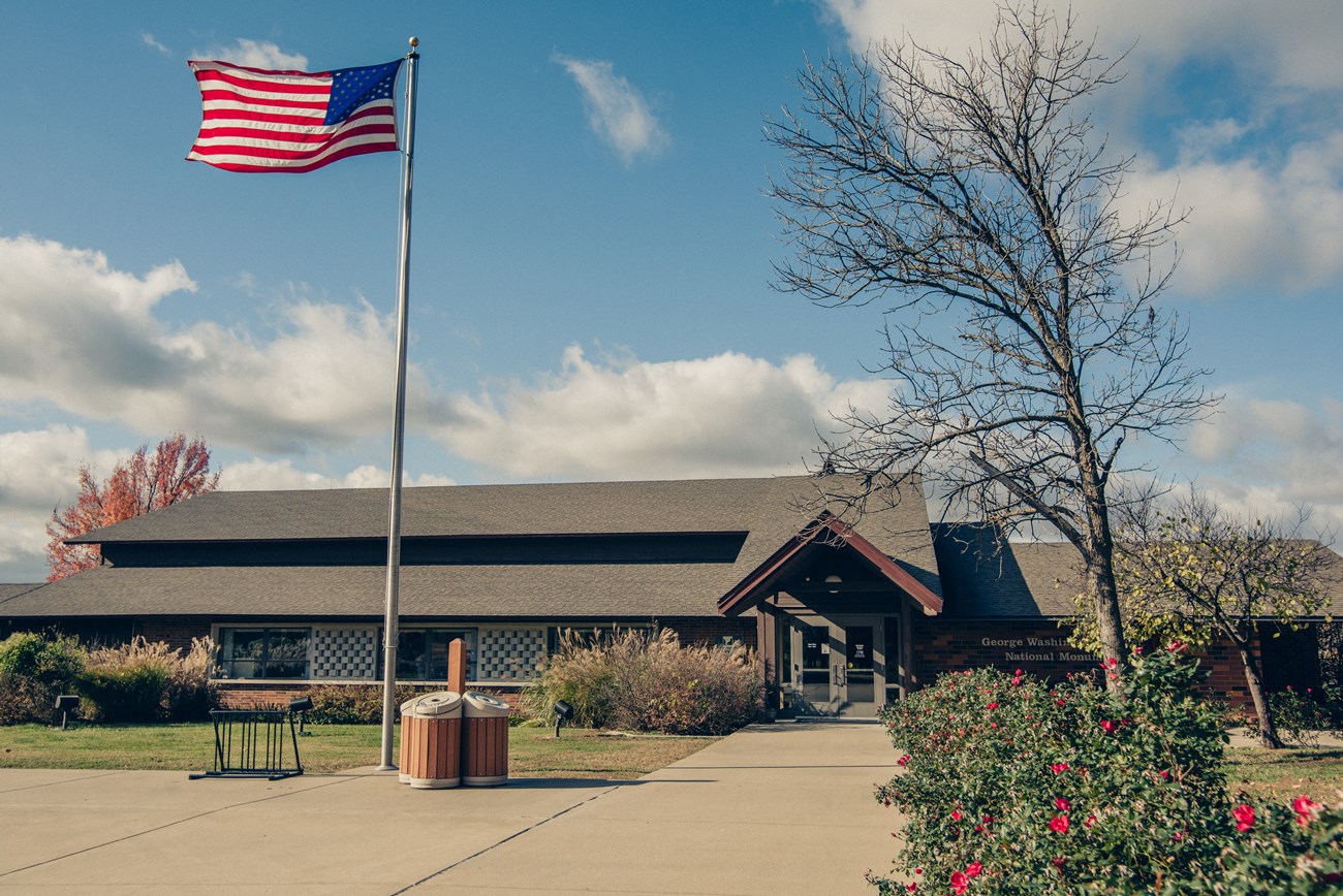 Visitor center building entrance with flagpole in the foreground and  landscaped with red roses.