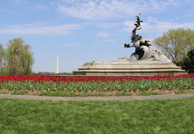 A statue of waves and gulls with red flowers in the foreground.