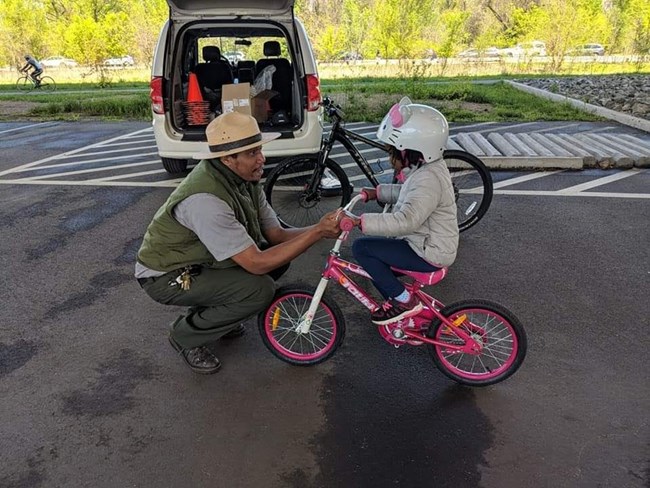A Park Ranger helps a child ride a bike.