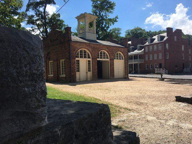 John Brown's Fort as seen from under the railroad overpass; it is a small brick building, with three doors, and a cupola atop it.