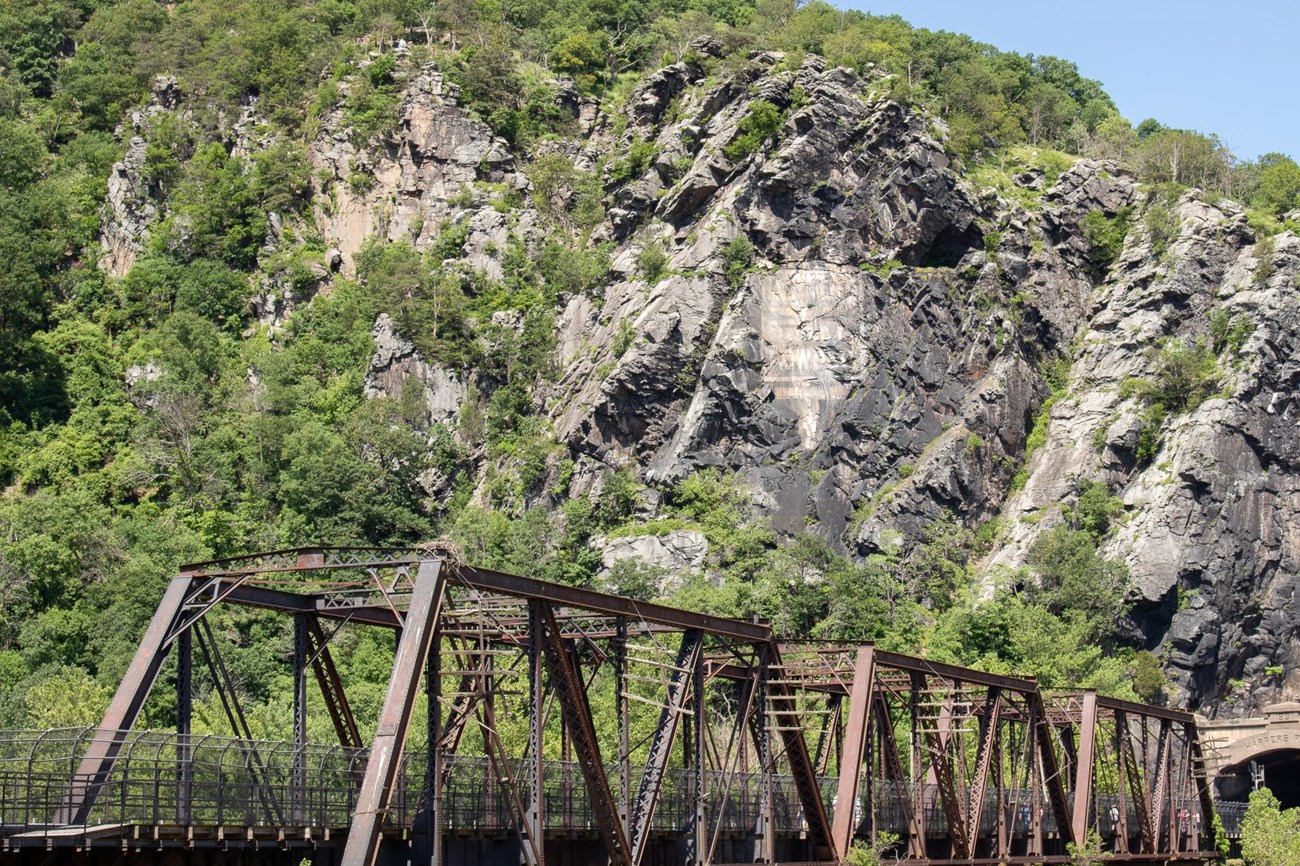 Rocky cliff face with illegible image above a train trestle bridge