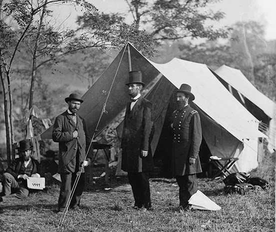 Abraham Lincoln and two other men stand near tents