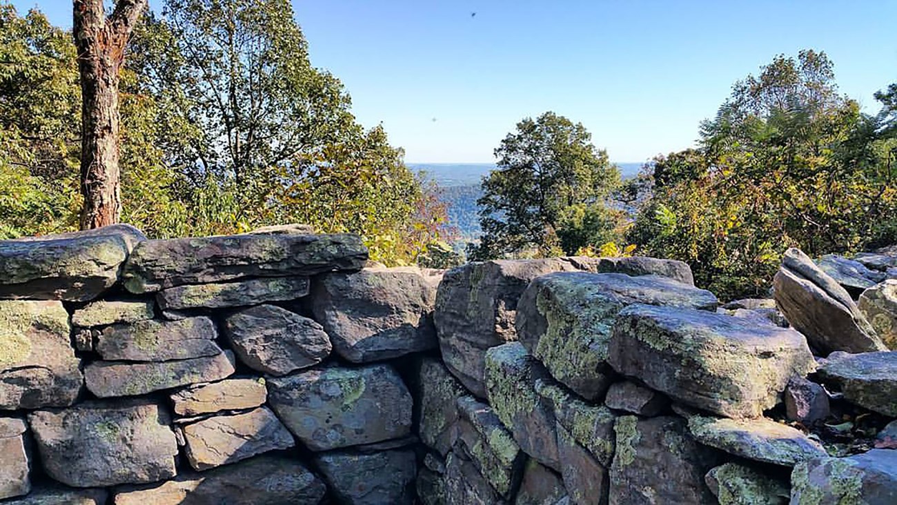Corner of stacked stone wall surrounded by trees at an overlook