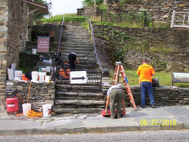 Staff work on stone steps. Tools and equipment lay around them.
