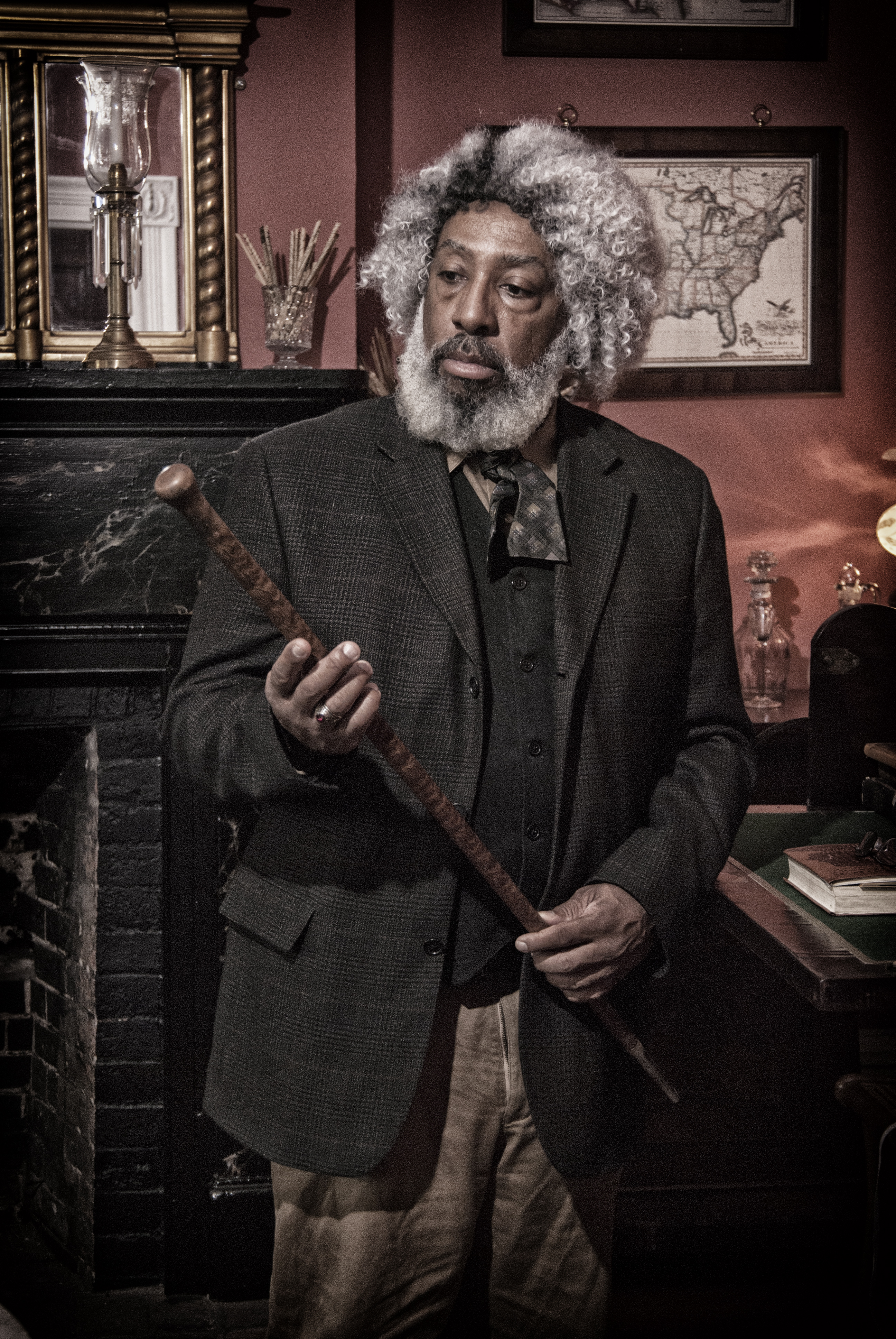 A man with gray hair and a beard, wearing a suit coat, looks at a staff in his hands.