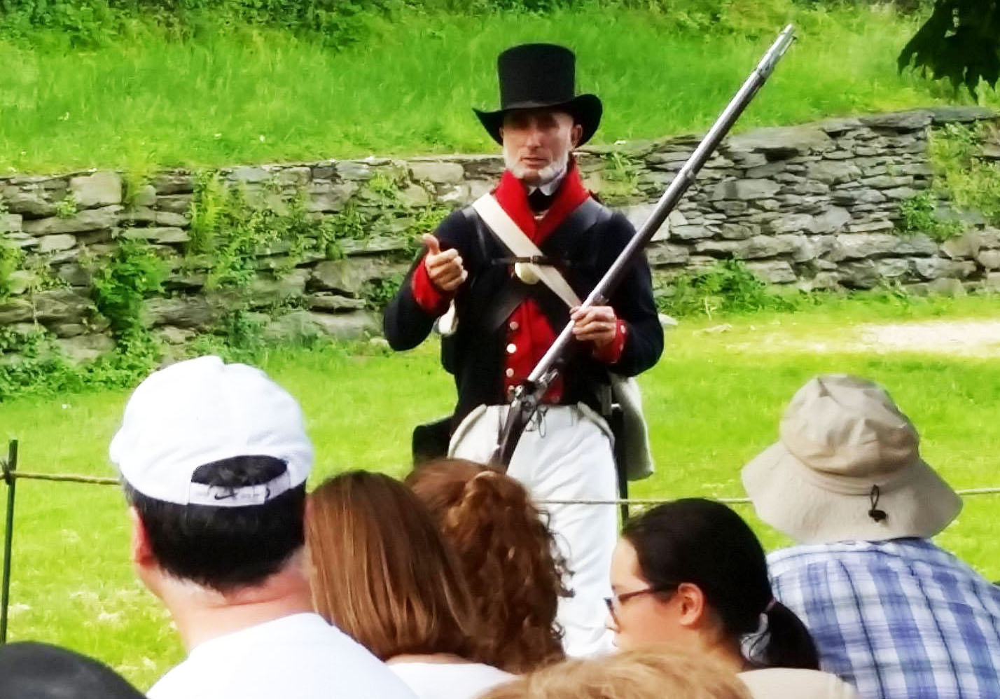 Male soldier wearing a blue, red, and white uniform with tall black hat holds a musket