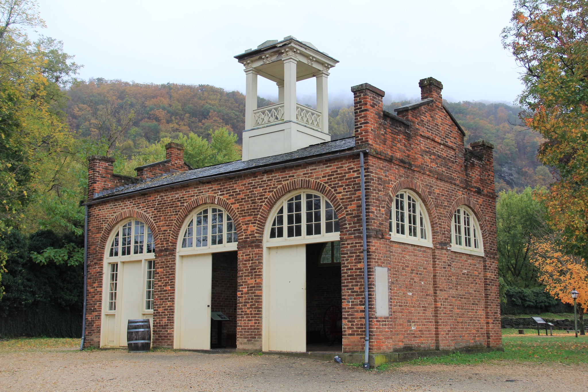 John Brown's Fort Rectangular brick building with central white cupola against an autumn wooded backdrop