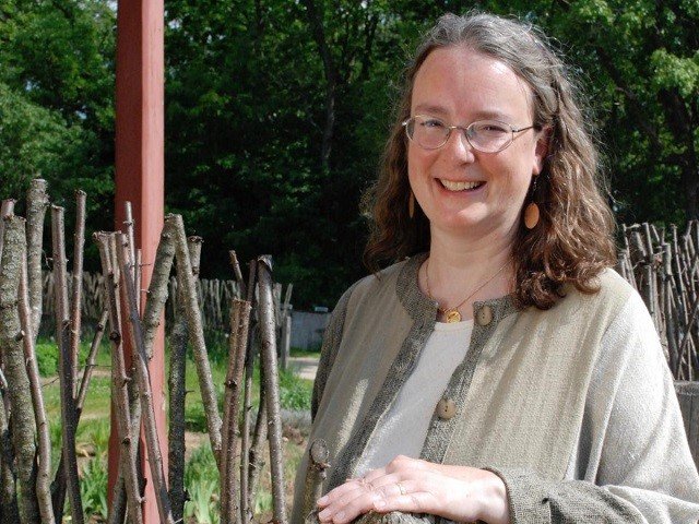 Woman with shoulder-length dark hair and glasses standing by a stockade fence