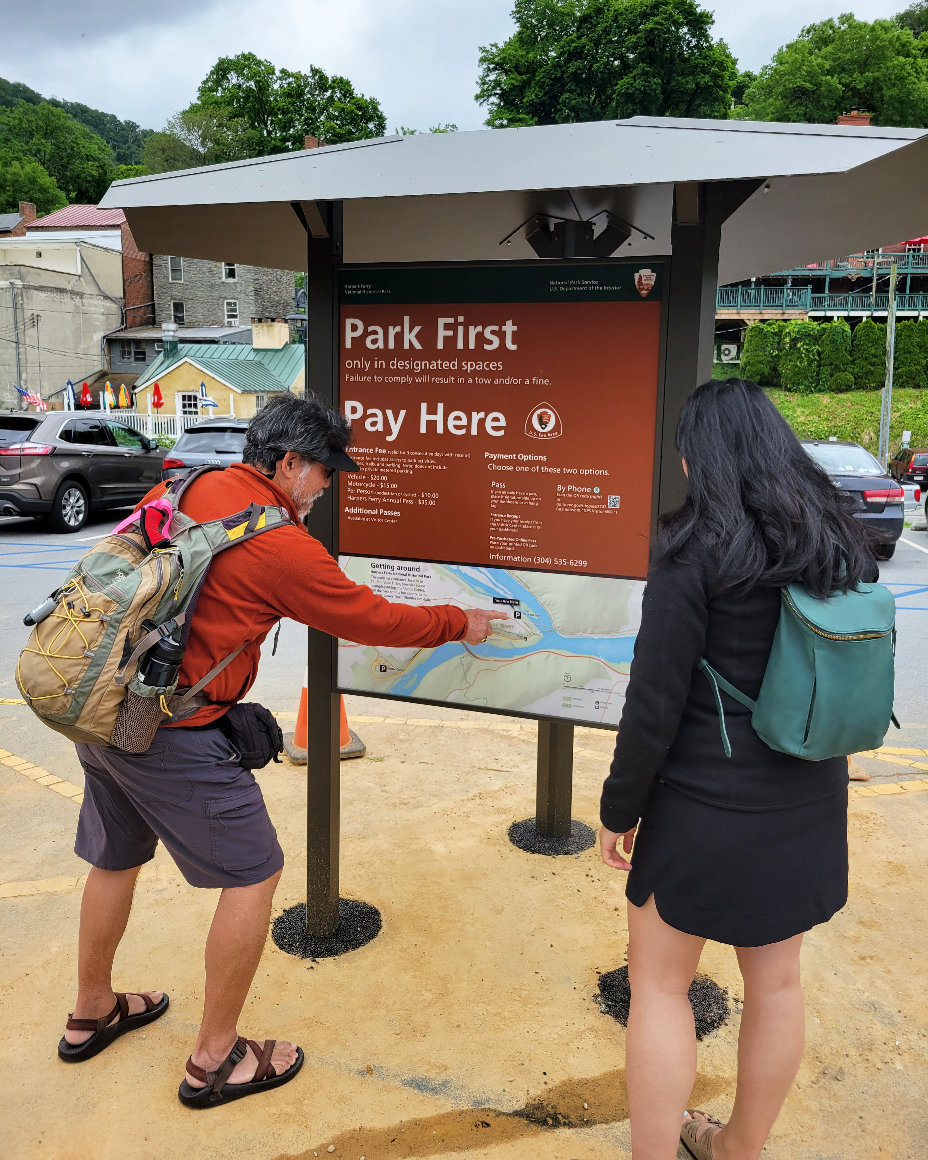 A man and woman stand in front of an informational kiosk, the man points at a map panel