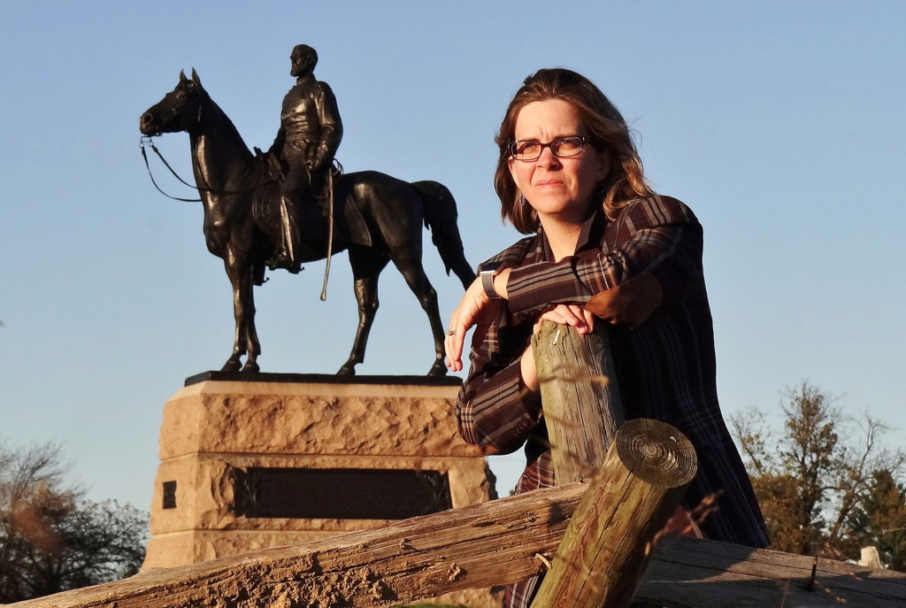 A woman leans on a fence in front of a statue of a man on a horse.