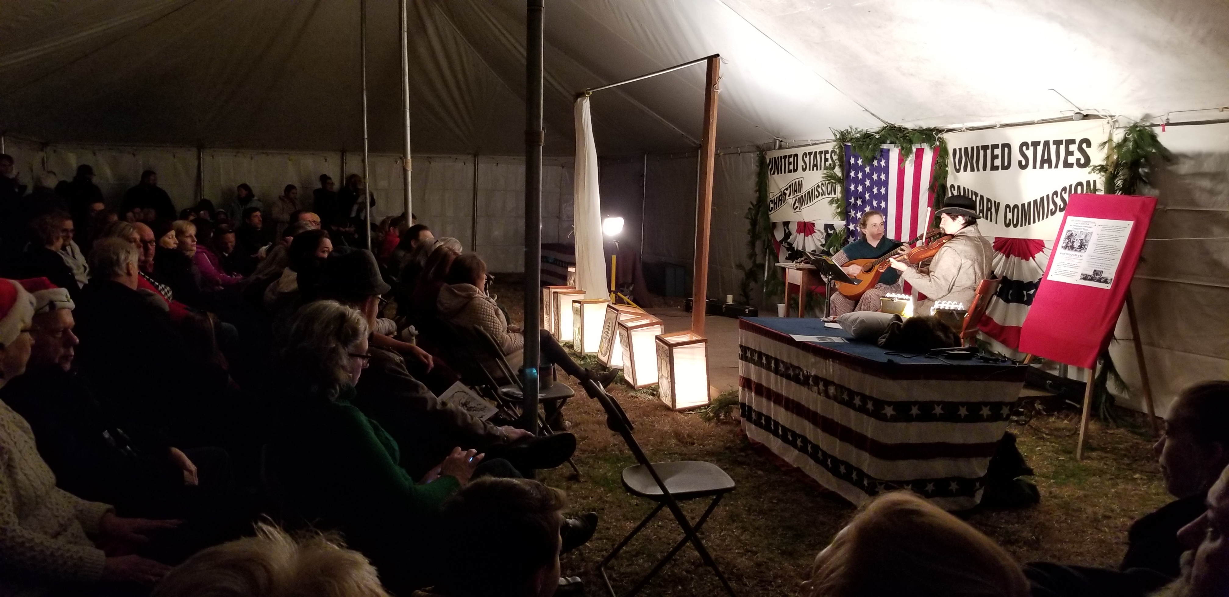 Capt Flagg Yultide opening ceremony A crowd sits in a tent watching two musicians play stringed instruments