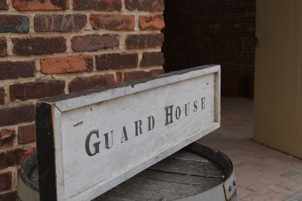 signs that reads "Guard House" atop a barrel in front of a brick building