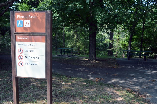 Sign indicating picnic area with picnic tables in the background.