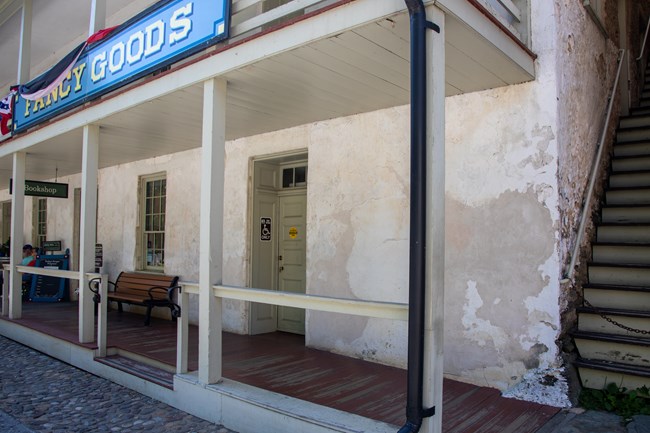 A building with a wood front porch and door with a sign for an accessible restroom.