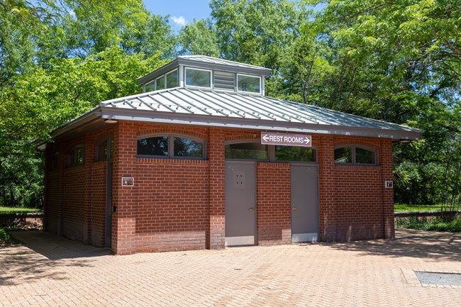 A single-story rectangular brick building with entrances to restrooms on either side.