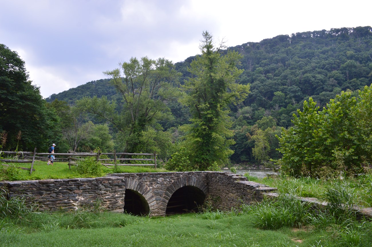 View along the Virginius Island trail of an old mill structure with two archways that water flows through.