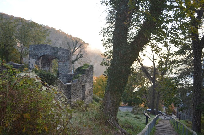 View of a church ruins, a sunlit bluff, and trees from a trail.