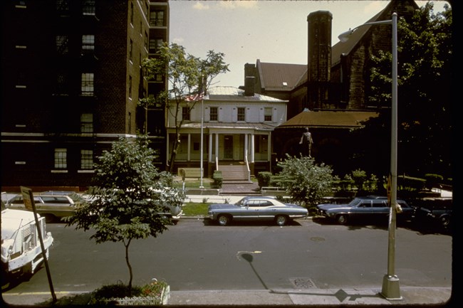 A small white house surrounded by large stone buildings.