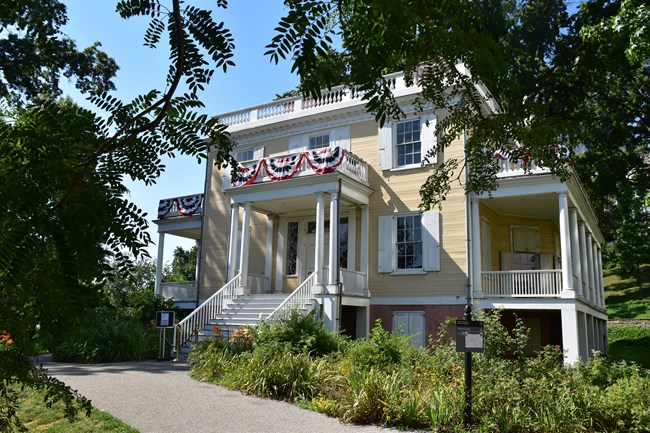 A yellow house with bunting, and surrounded by trees.