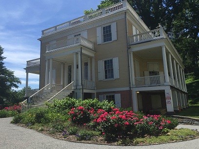 A yellow house stands behind gardens with roses.